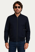 Giubbino Giacca Antivento Nylon in blu, abbinato a jeans, con occhiali da sole, modello maschile, look moderno.